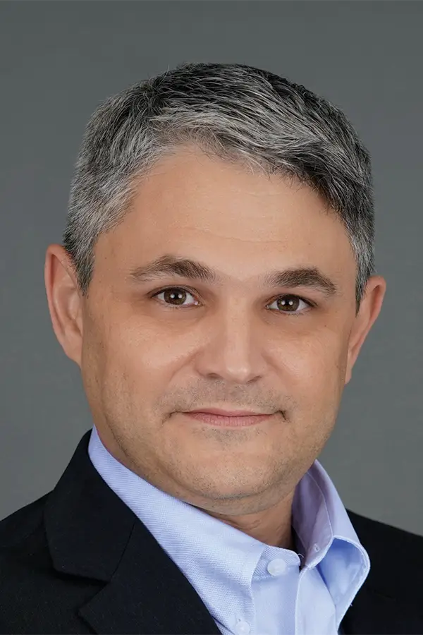 Portrait of a man with short gray hair, wearing a dark suit and light blue shirt.