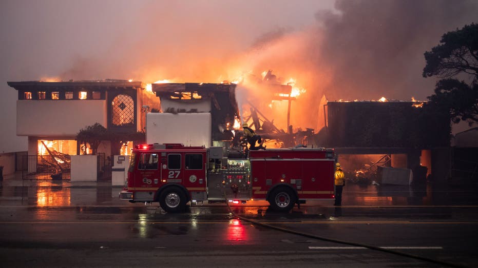 Fire truck parked in front of a burning building at night.