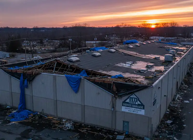Aerial sunset view of tornado-damaged commercial warehouse with blue tarps