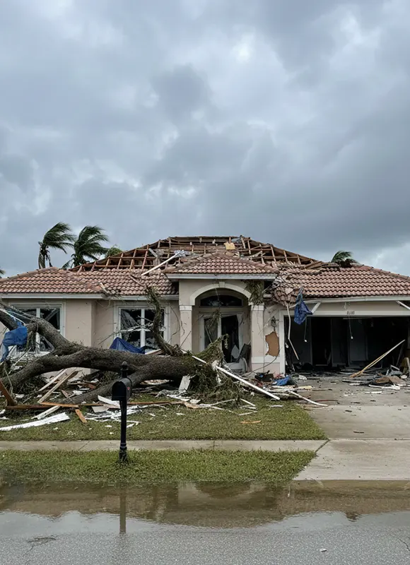 Large tree crushing front entrance of hurricane-battered Florida tile-roof home